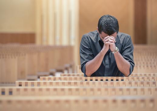 Young beard man wearing blue shirt praying in modern church.